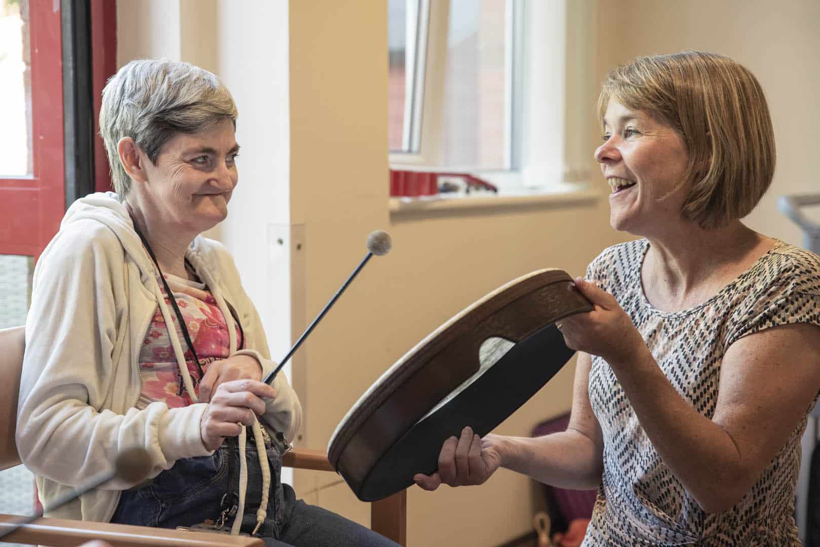 Two people excitedly sit down together to play music on a drum during a music therapy session at Enable Glasgow.