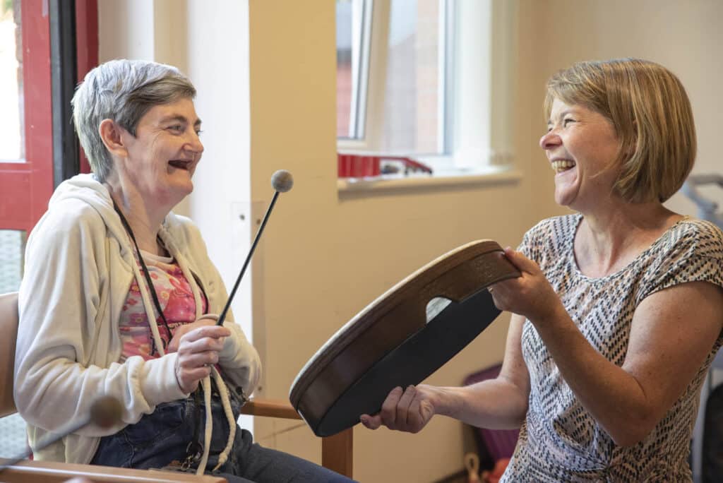 Two people laugh as they play the drum together during a music therapy session at Enable Glasgow.