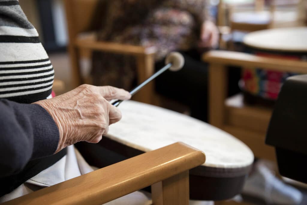 With a drumstick in their hand, a person reaches towards a drum to play music during a music therapy session.