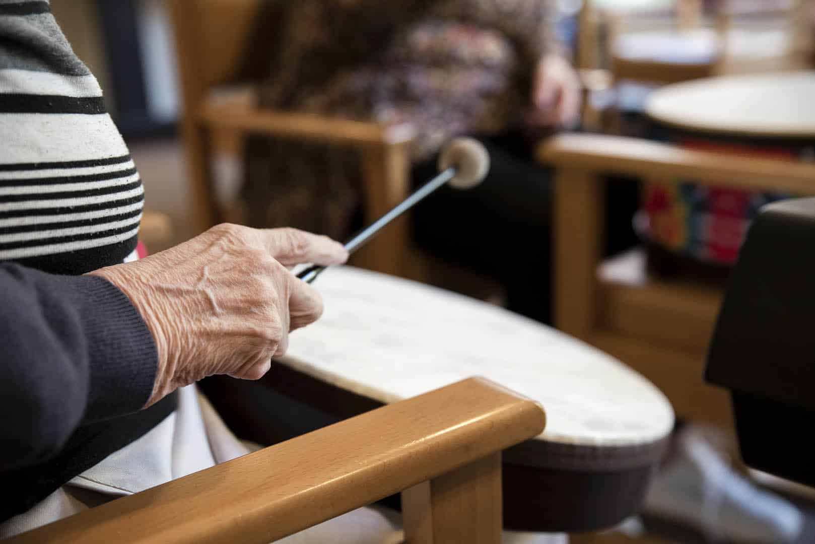 With a drumstick in their hand, a person reaches towards a drum to play music during a music therapy session.