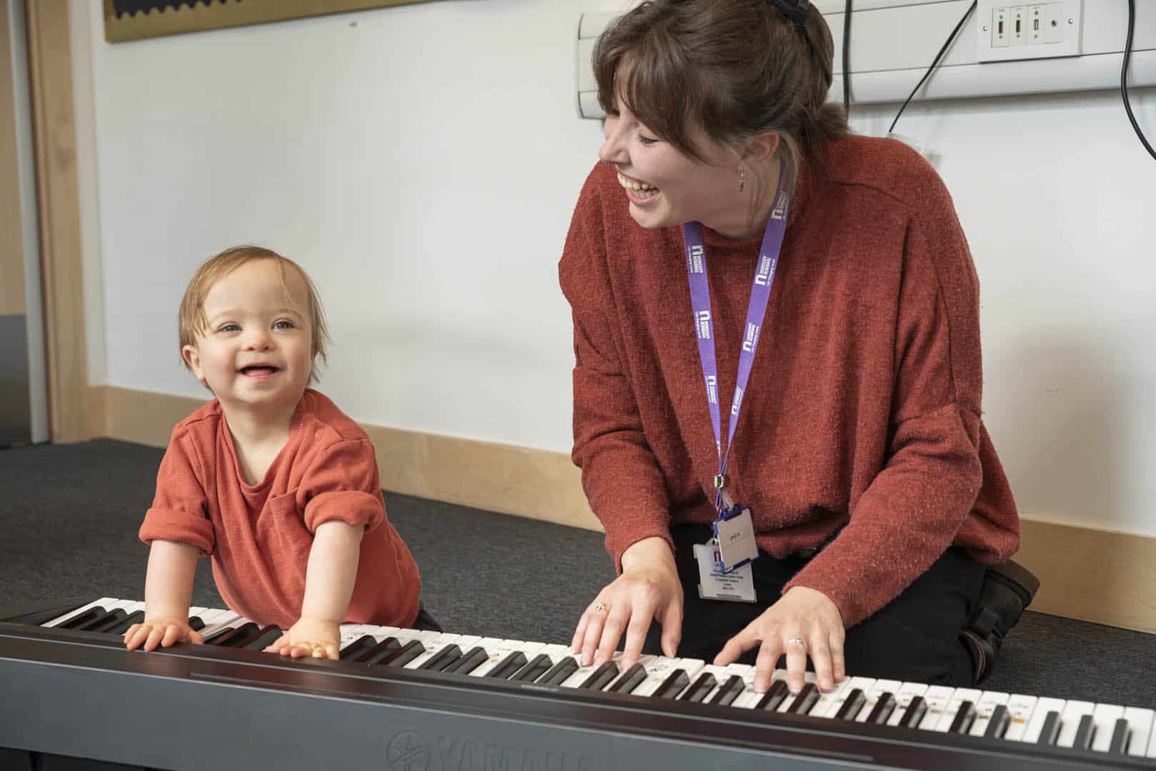 Together, a young child and music therapist happily play the keyboard during a music therapy session