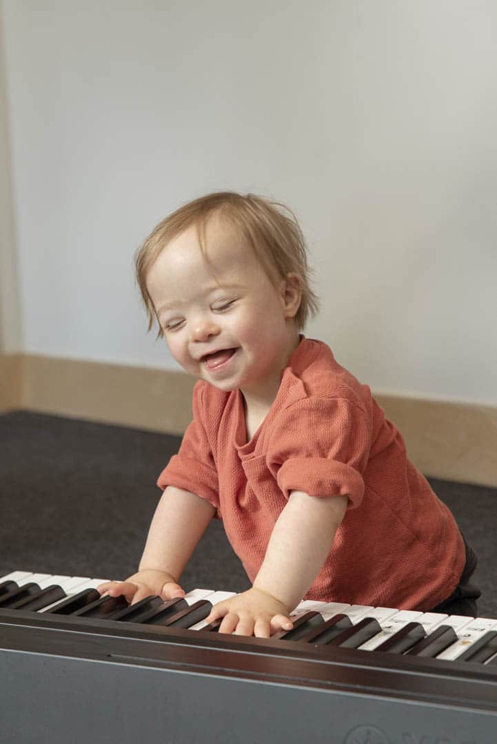 A young child laughs, placing their hands on a keyboard during a music therapy session at a Nordoff and Robbins partner organisation.