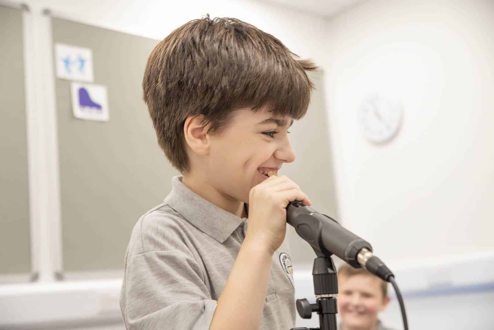 During music therapy at one of our partner schools, a smiling young client smiles performs at a microphone