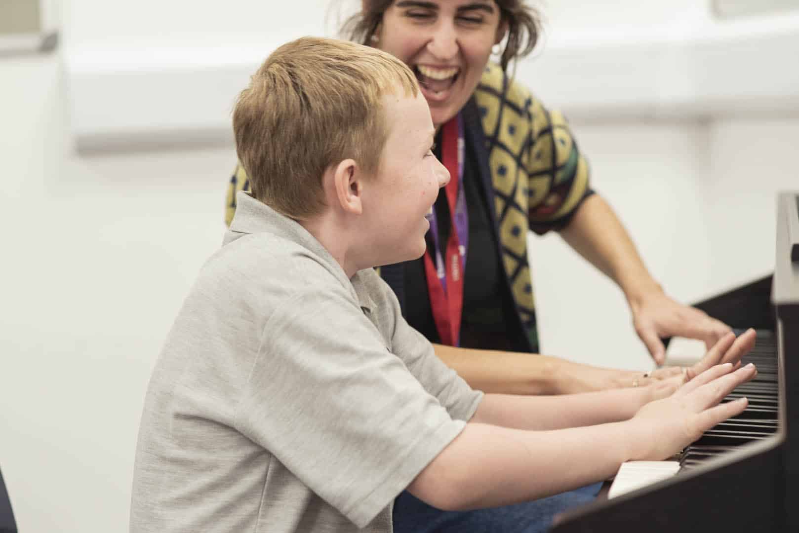 A young client and music therapist are excited as they play the piano together during a music therapy session