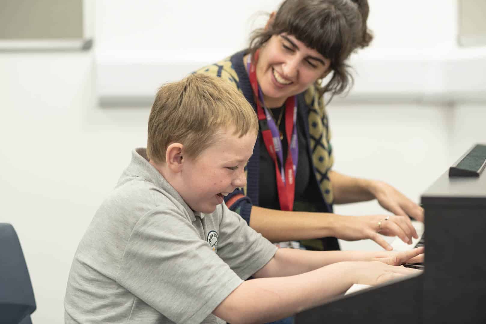 Together, a young client and music therapist cheerfully play the piano together at one of Nordoff and Robbins' partner organisations.