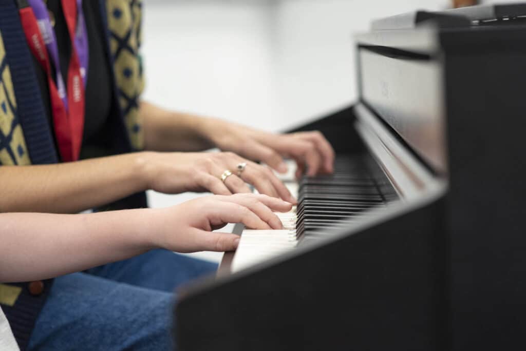 A music therapist and client sit together, playing music on the piano during a music therapy session