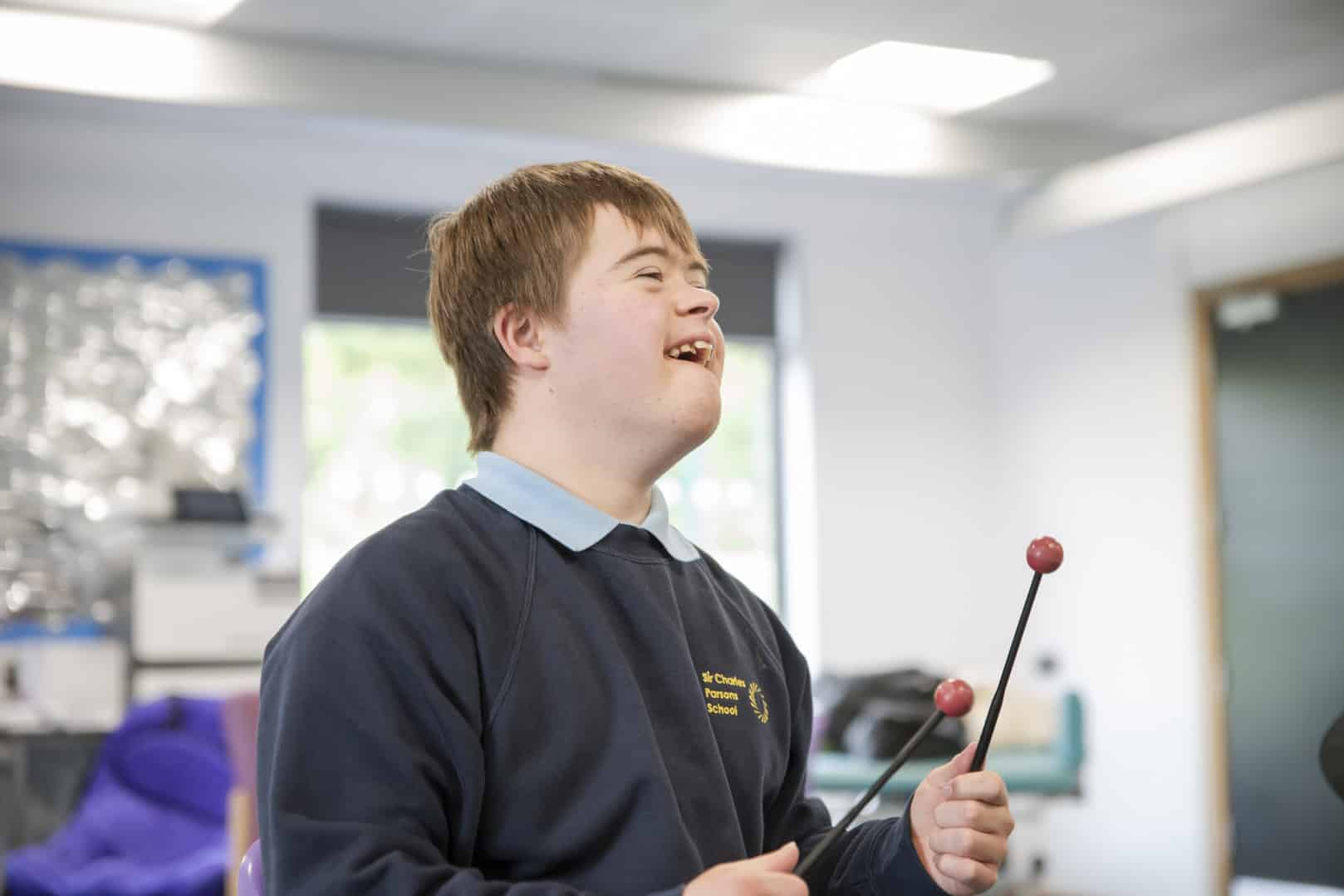 As music therapy takes place at one of our partner schools, someone excitedly stands up holding a pair of drumsticks