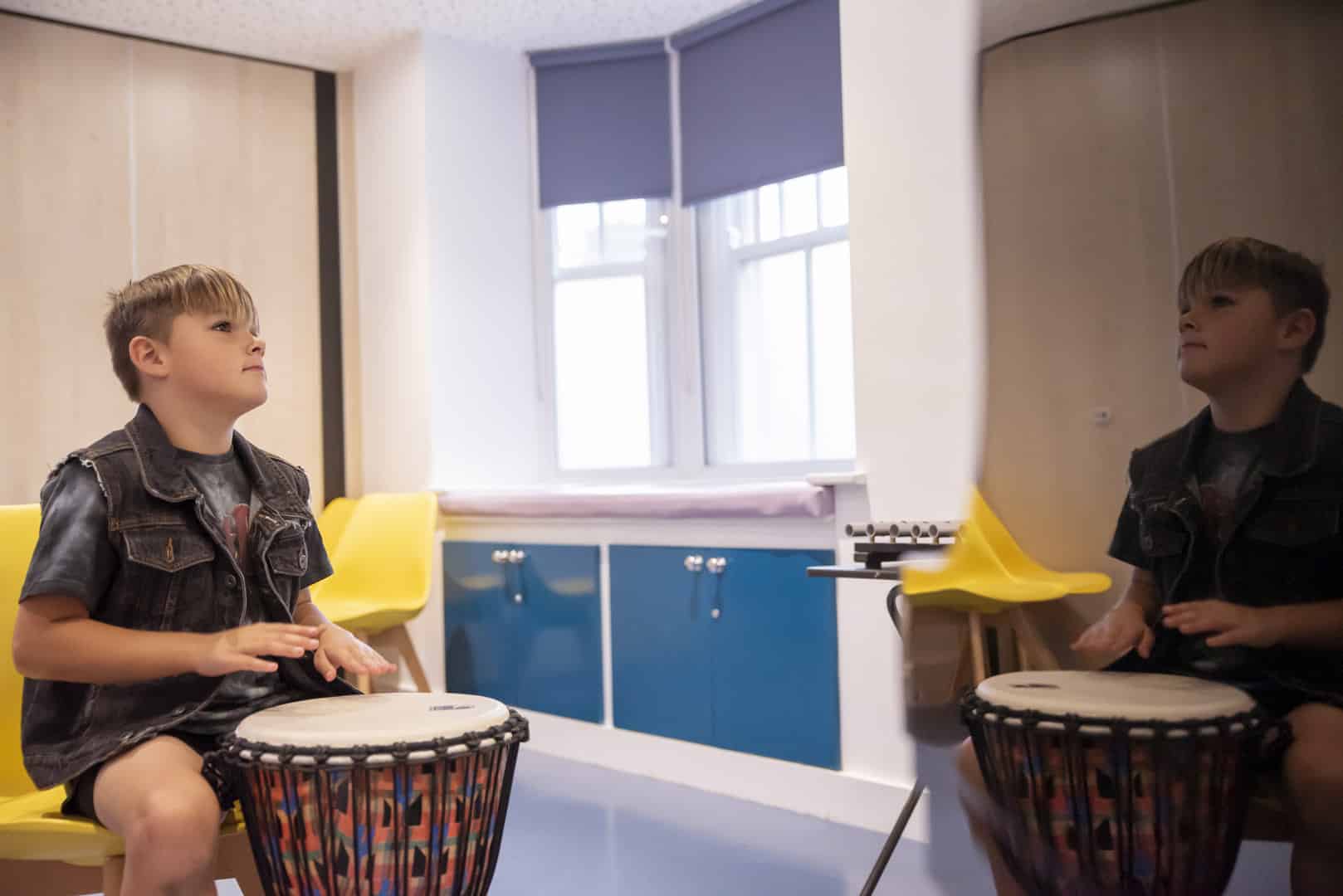 A young person is focussed as they sit down and play music on a drum at one of our partner schools