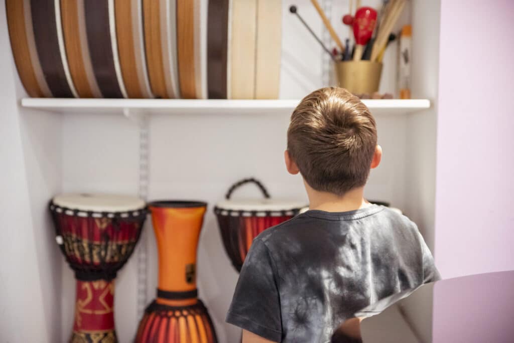 A young person looks at the drums in a musical instrument cupboard, deciding which one they should choose