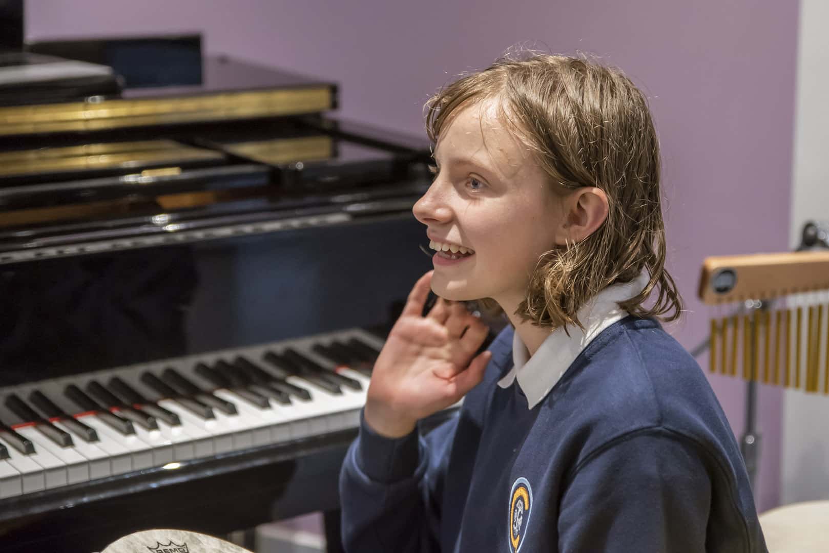 A young music therapy client sits smiling at a piano at a Nordoff and Robbins partner organisation