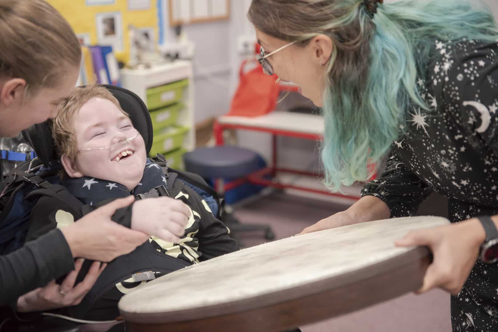 During music therapy at one of our partner schools, a young person laughs and smiles, as someone holds out a drum to them