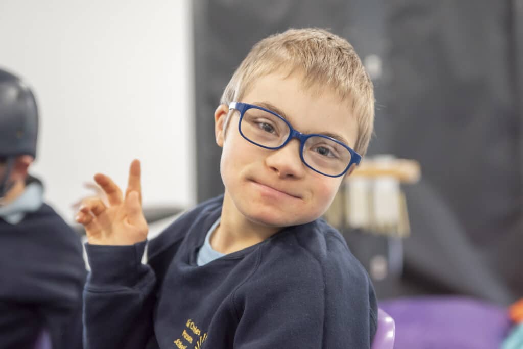 A client who is a child attends a music therapy session, looking at the camera with his hand in the air.