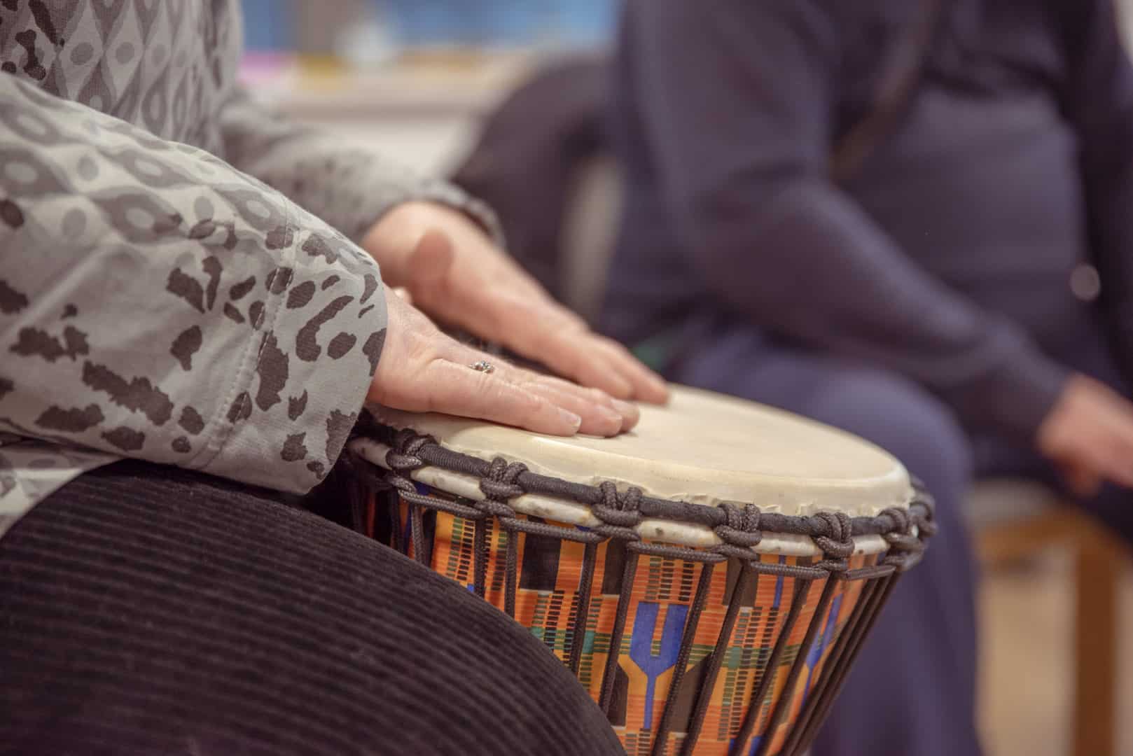 Someone plays music on a drum, as they sit down with other people to take part in a music therapy session