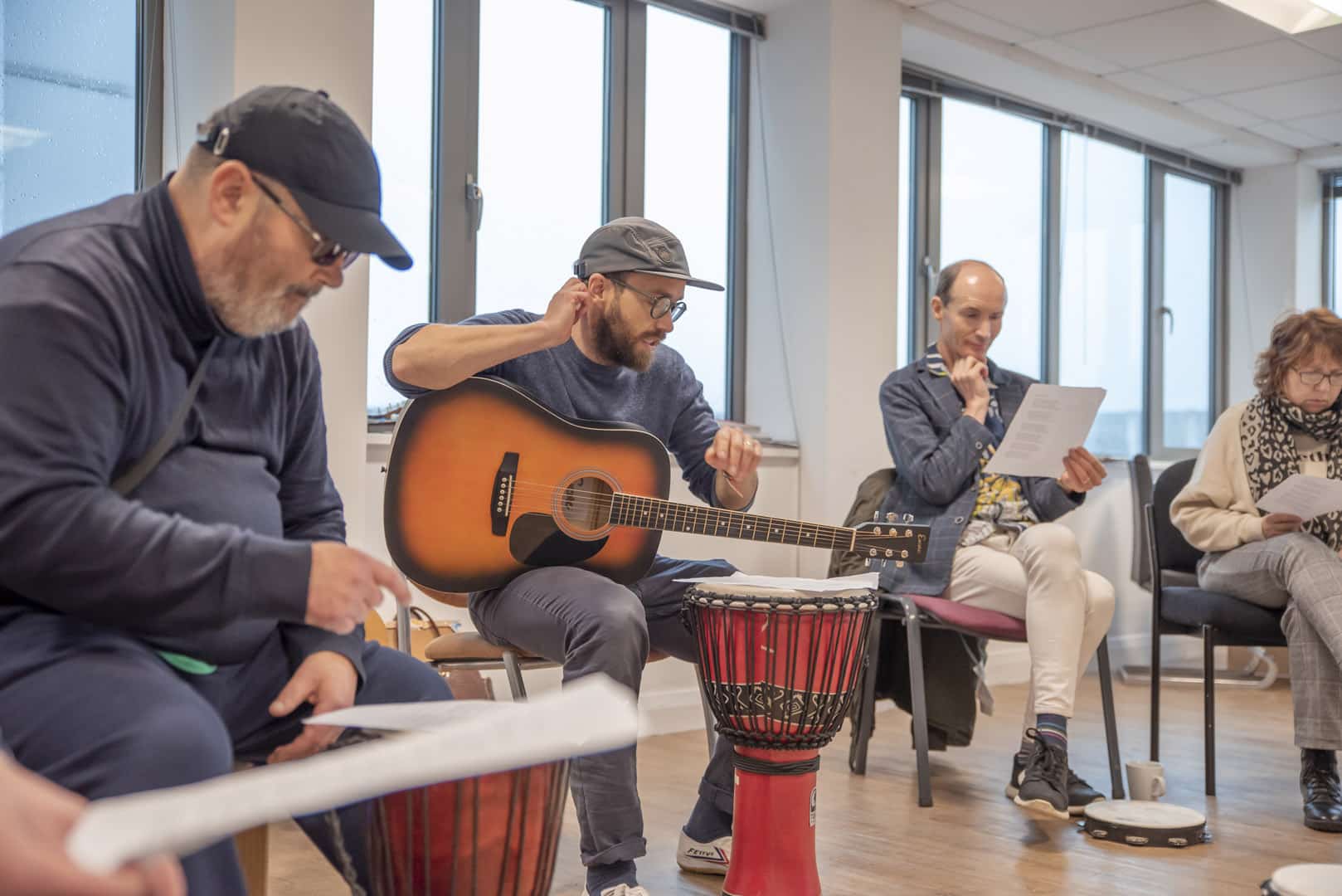 A group of people look down at lyric sheets, as they come together to take part in music therapy at one of partner prganisations, ReCoCo