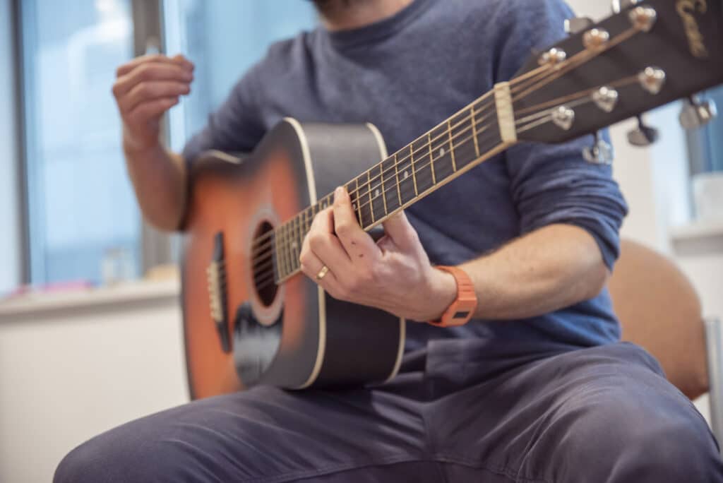 A music therapist plays music on their acoustic guitar, as they take part in a music therapy session