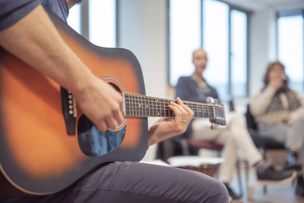 A music therapist sits down to play music on the acoustic guitar, during a group music therapy session