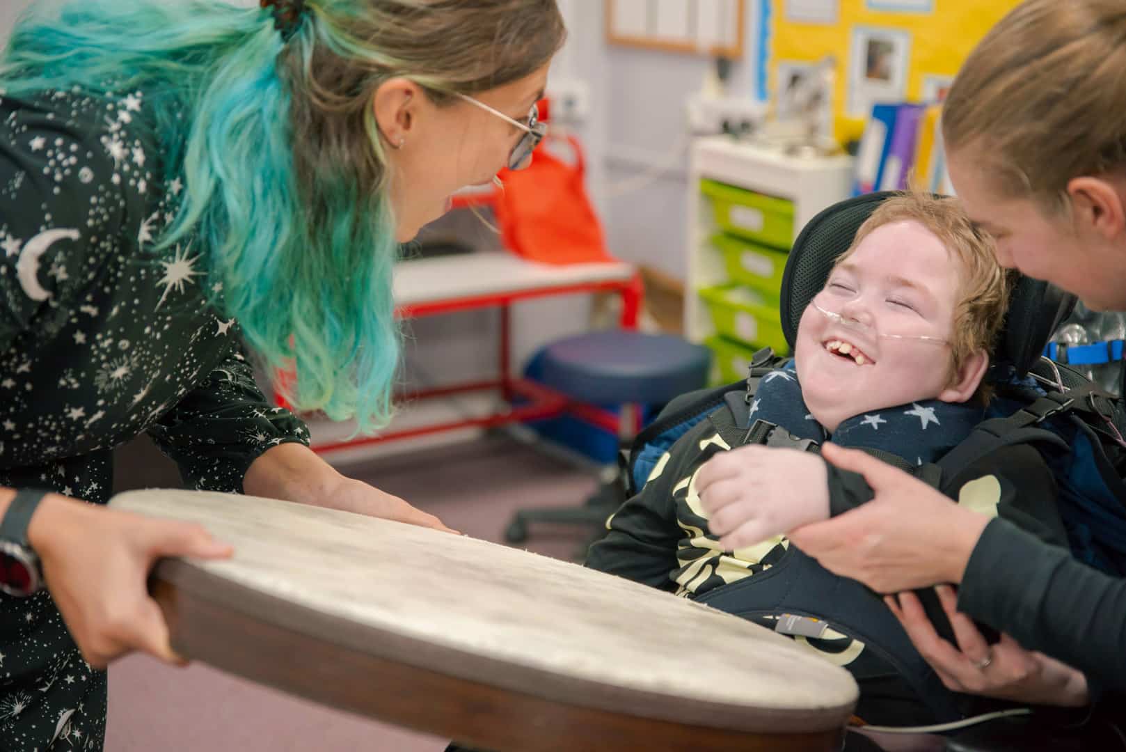 A happy client takes part in a music therapy session at one our partner schools, laughing as someone holds out a drum for them to play.