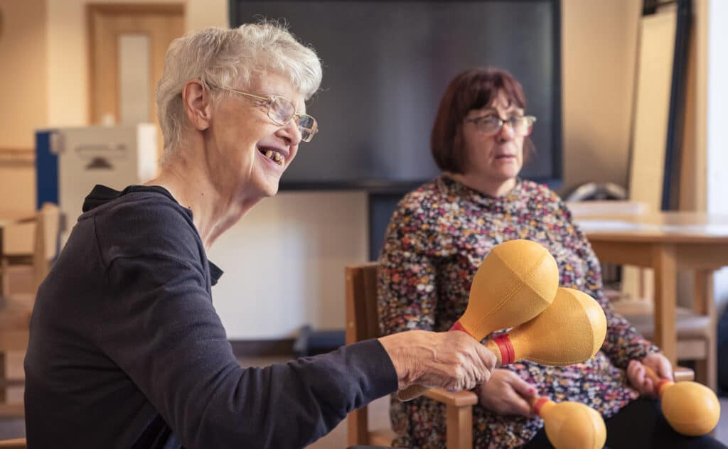 Janet happily smiles during a music therapy session at Enable Glasgow, as she shakes a pair of maracas.