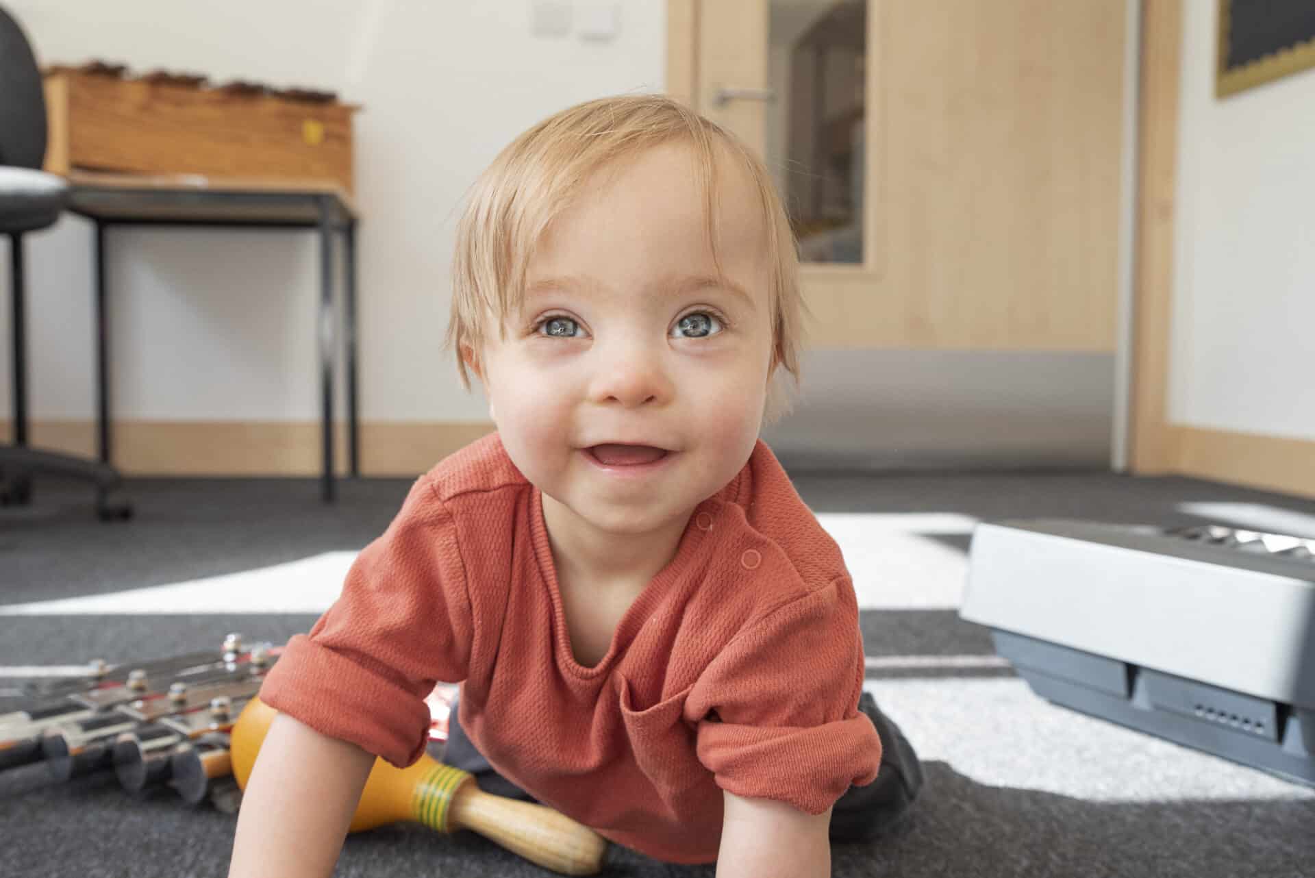 A young child crawls across the floor among during music therapy, musical instruments on the floor beside them.