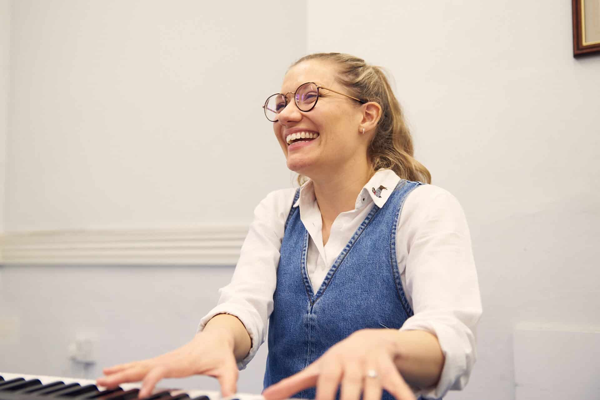 A person plays music on a keyboard, as they laughing and smiling during a music therapy session at a Nordoff and Robbins partner organisation