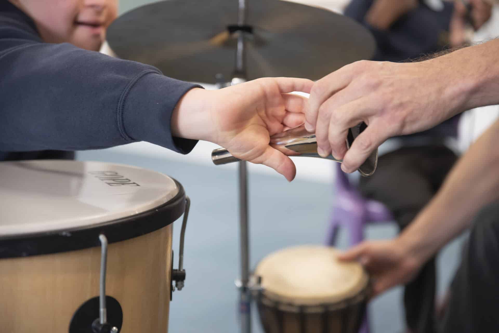 A young client extends out their arm to take a small silver horn instrument, as someone passes this to them