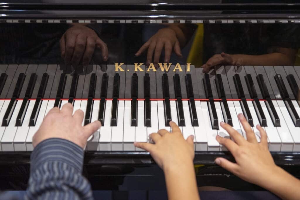 A young client and music therapist sit together at a piano, playing music together during music therapy.