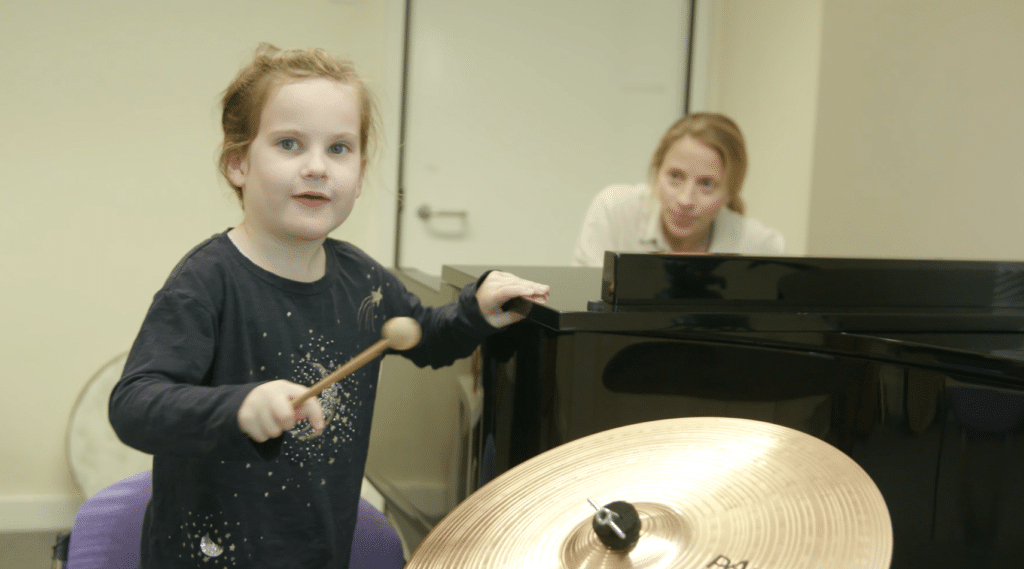 Patsy takes part in music therapy, holding a drumstick as music therapist Harriet is plays the piano