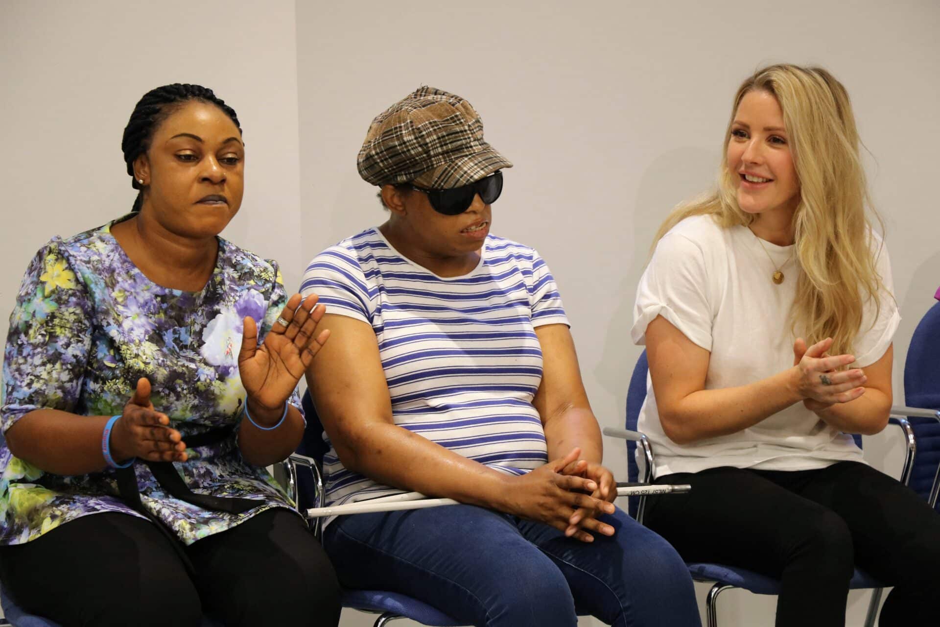 Ellie Goulding joins a music therapy session with a client and their family member who are each clapping together.