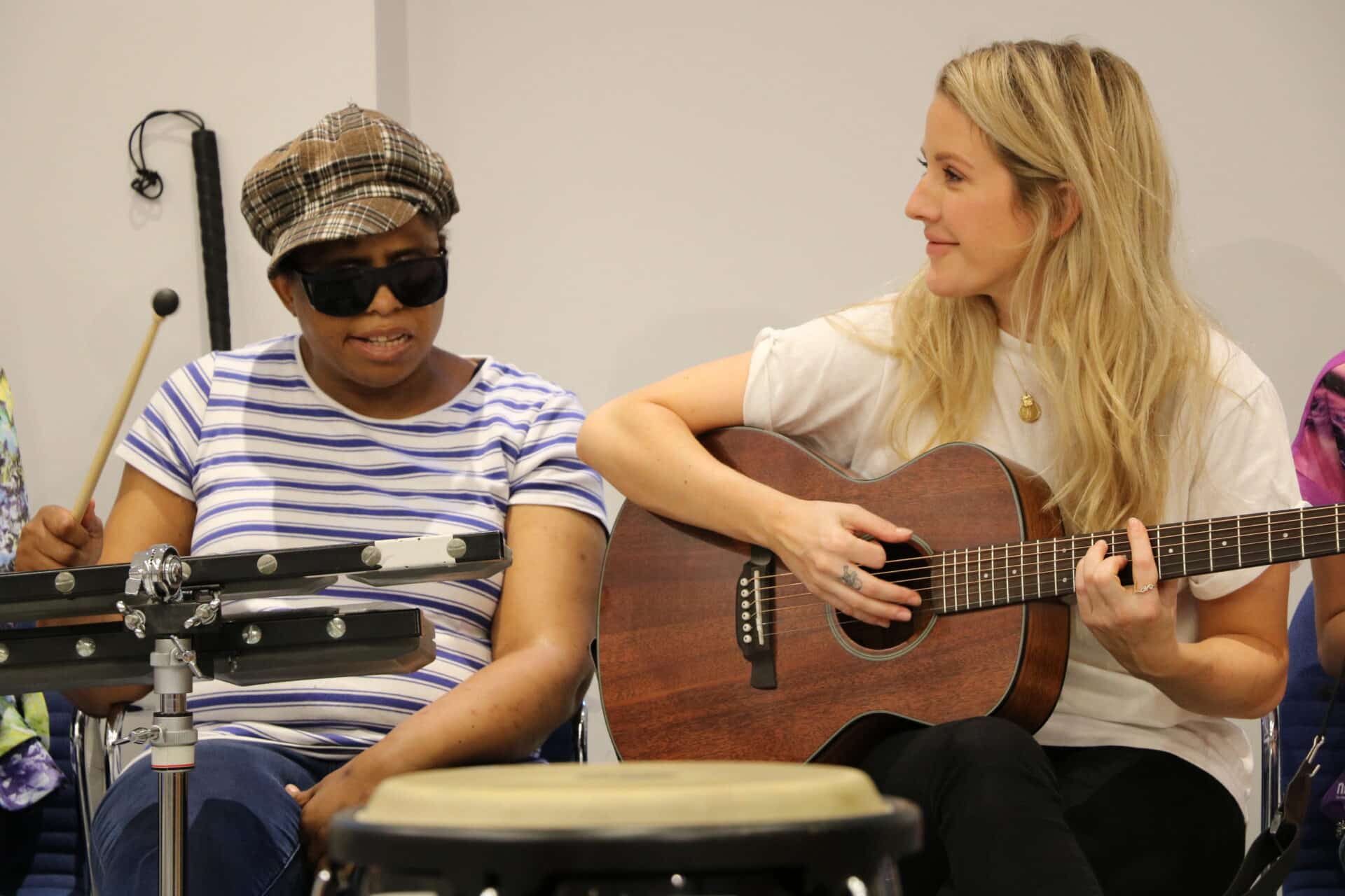 A music therapy client plays an electric drum kit, seated next to singer Ellie Goulding as she plays the acoustic guitar.