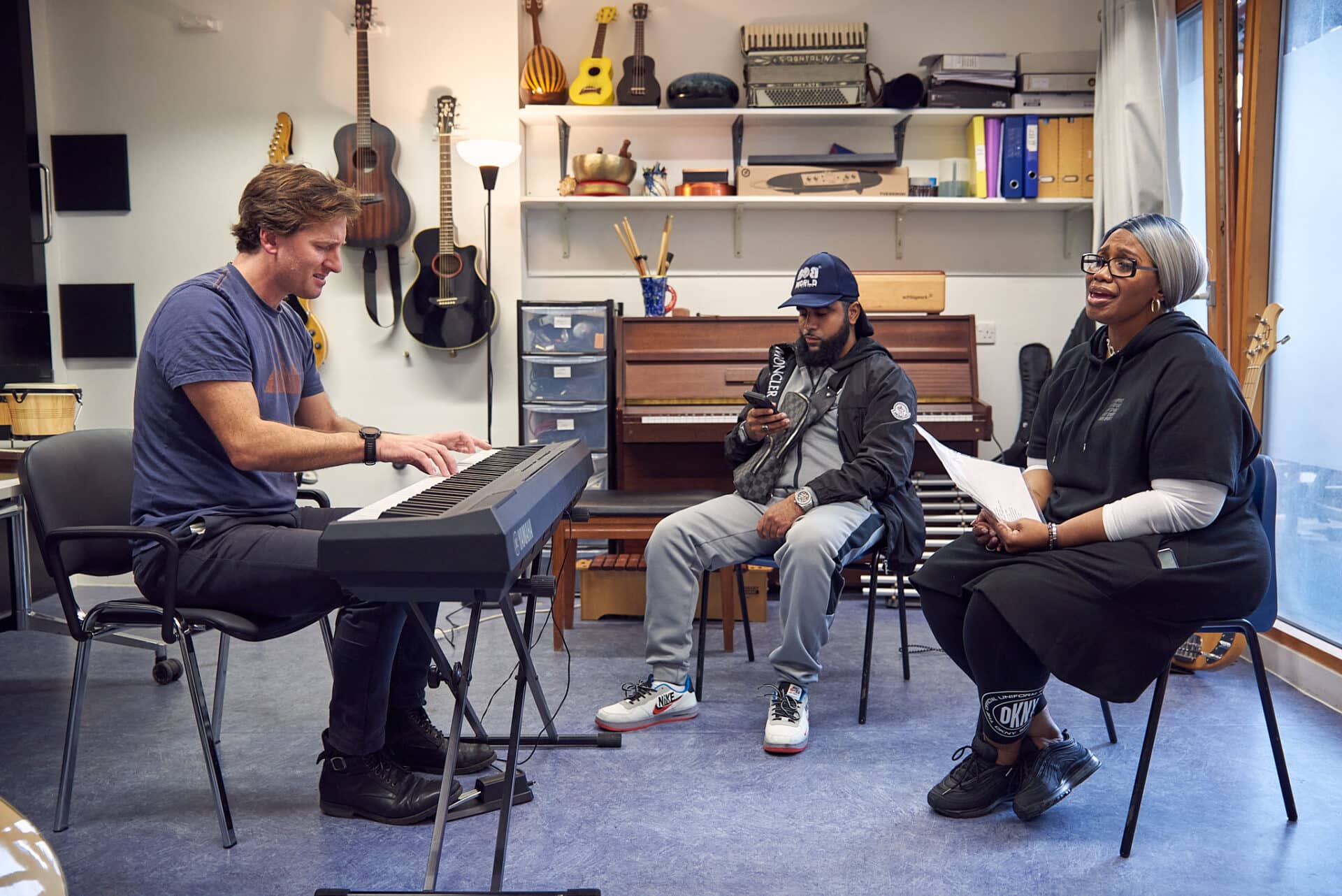 Two people sing passionately during a music therapy session, at Headway, a Nordoff and Robbins partner organisation. Music therapist Oli joins in as he plays the keyboard.