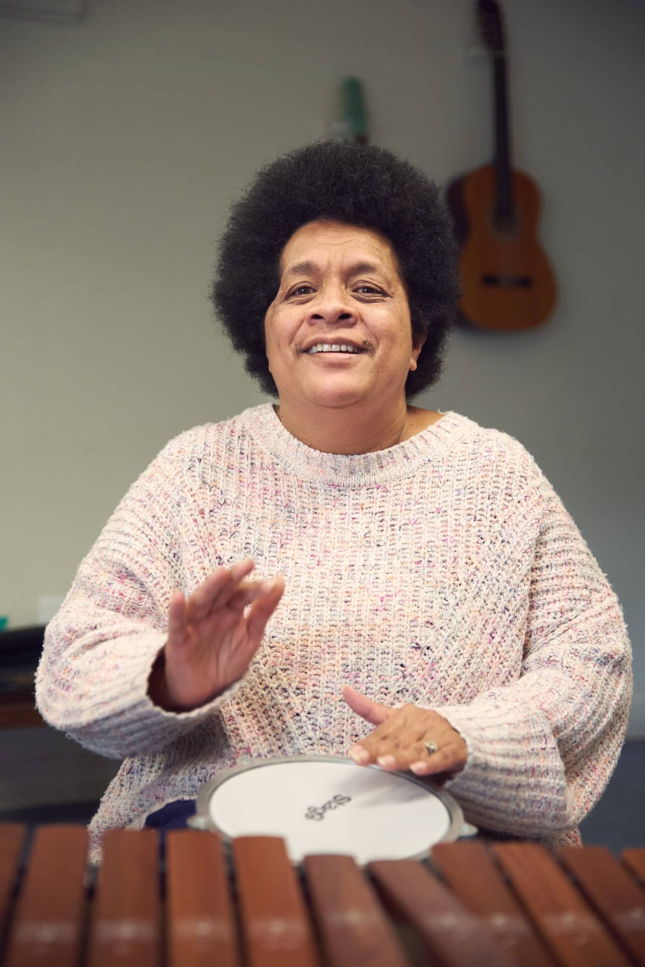 Cheerfully hitting a drum, a person sits surrounded by instruments during music therapy at Headway.