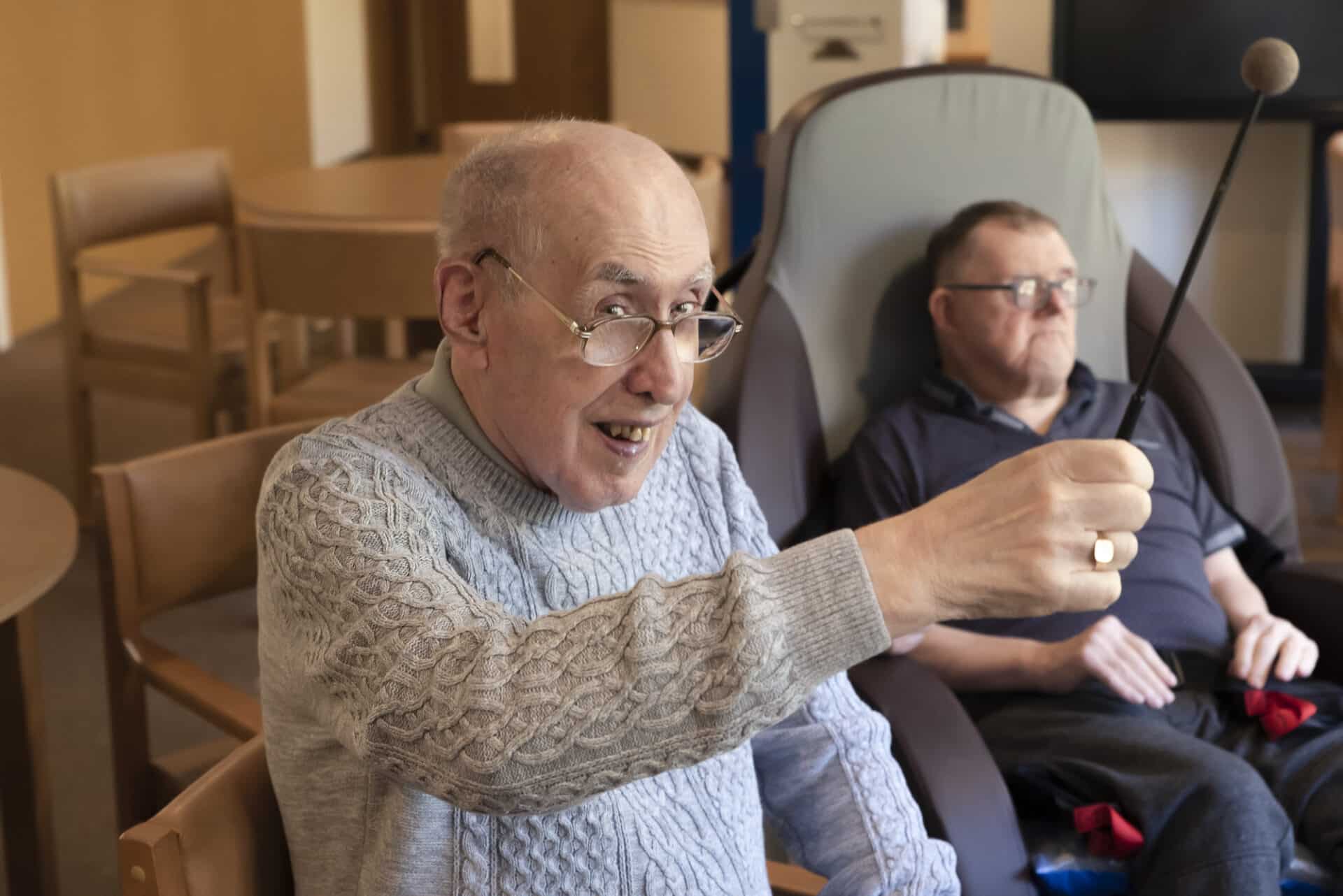 A smiling client holds up a drum stick during music therapy at Enable Glasgow.