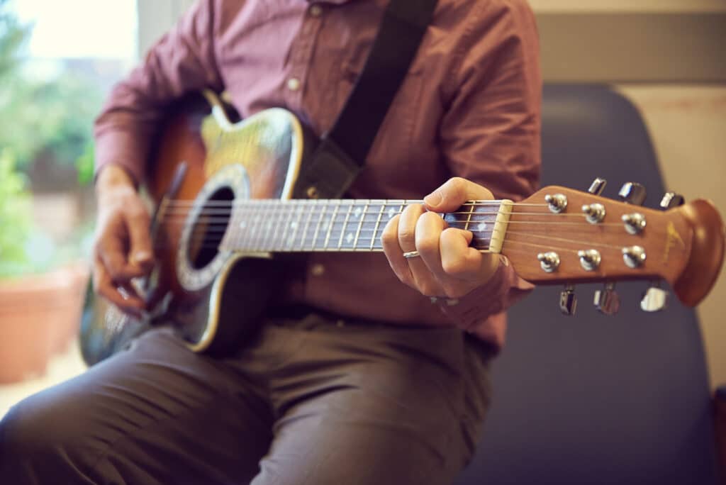 During a music therapy session, a music therapist sits down to play music on an acoustic guitar
