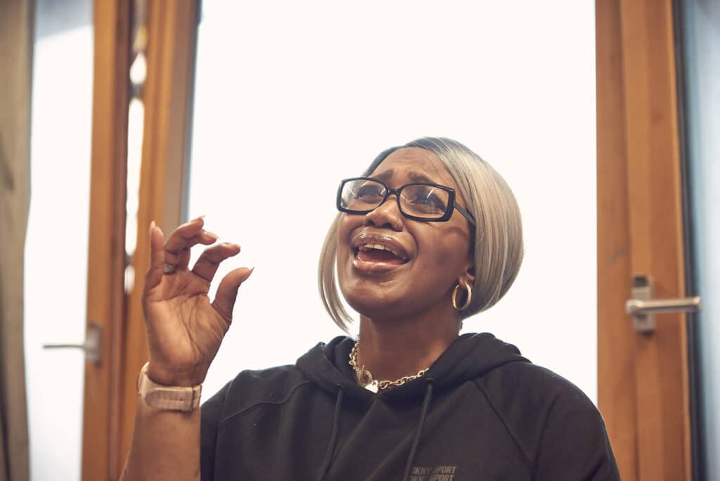 With their head raised upwards, a person lifts up their hand as they sing passionately and emotively.