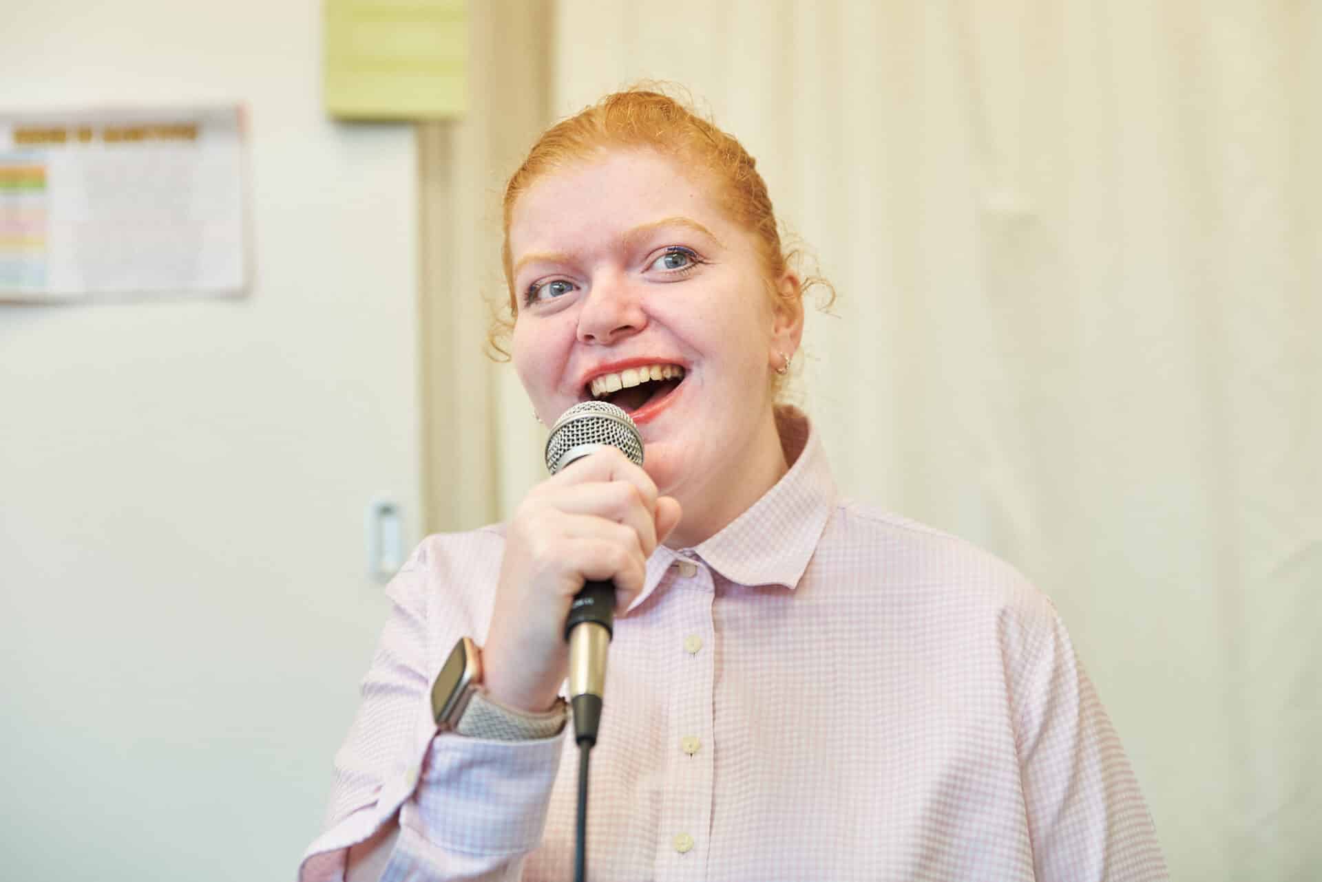 A person smiles whilst vocalising into a microphone during a music therapy session.