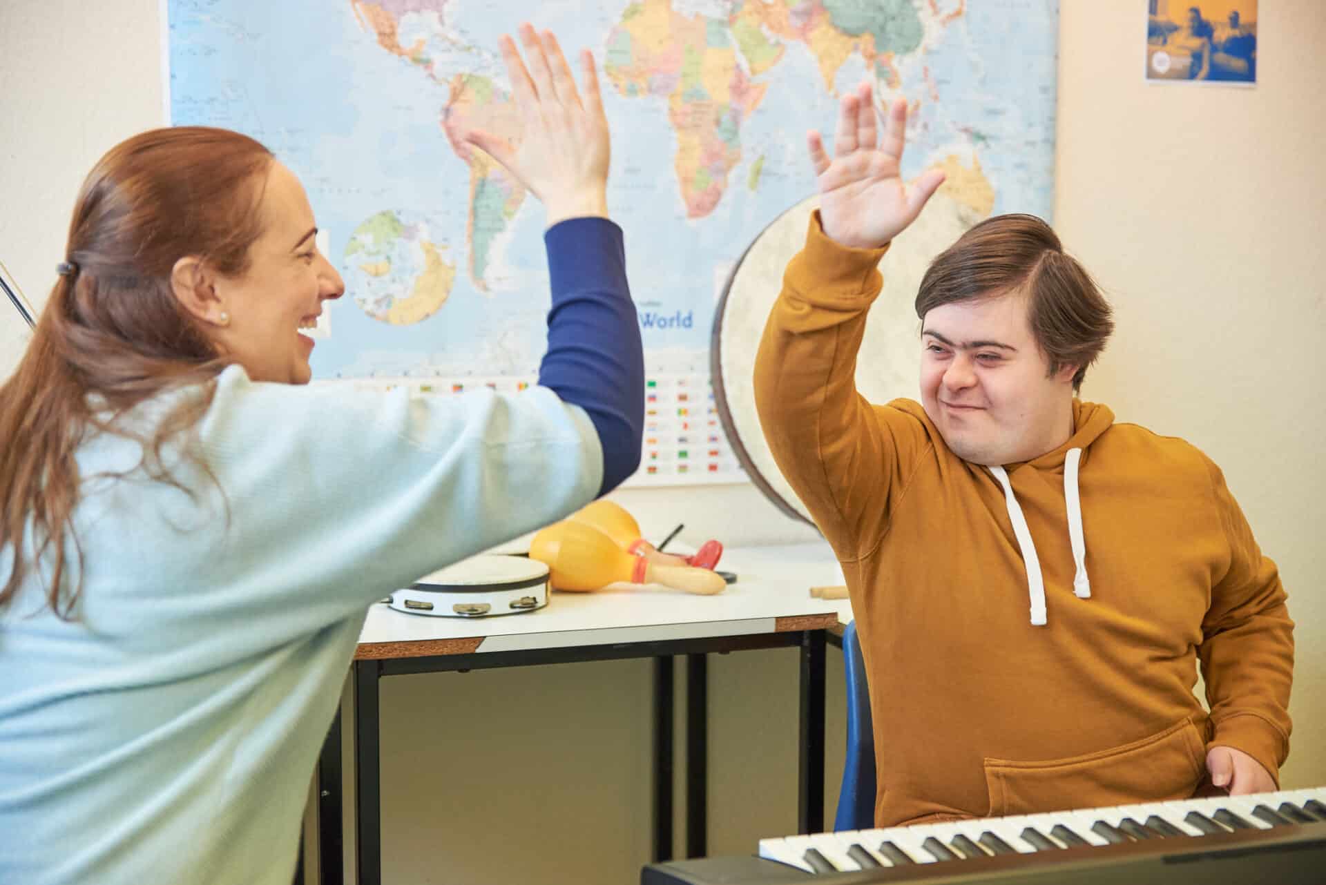 A music therapist and client high five each other whilst smiling and sitting in front of an electronic keyboard.