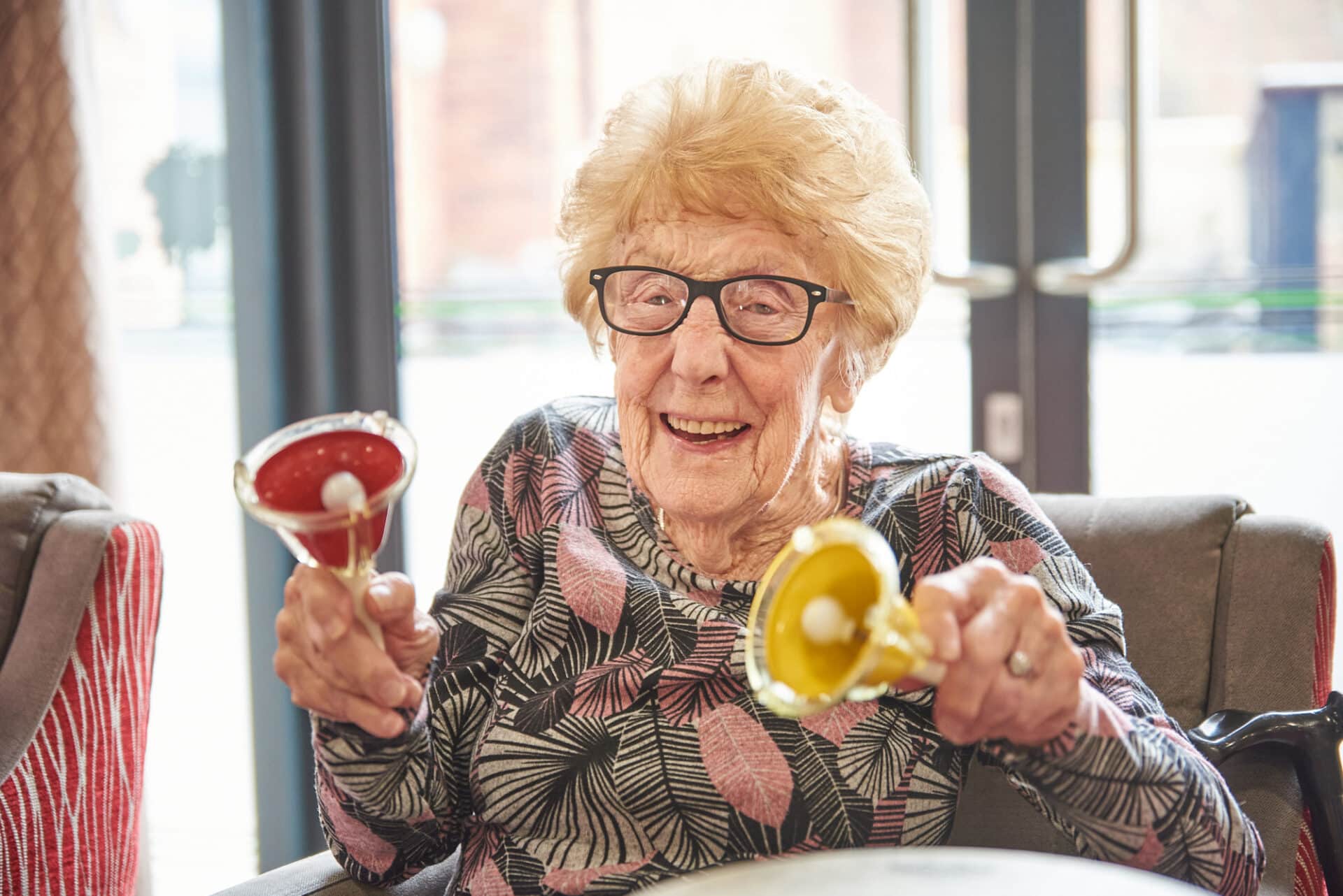 A cheerful person smiles during a music therapy session as she plays two handheld bell instruments.