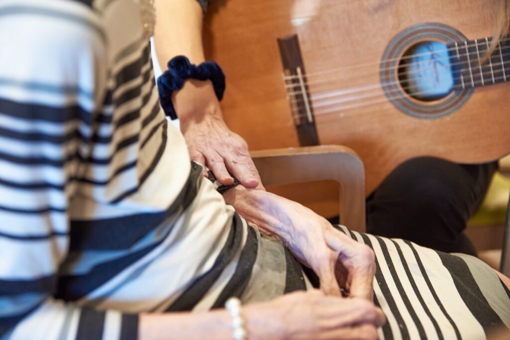 A music therapist playing the guitar extends her hand to an elderly client's arm during a music therapy session.