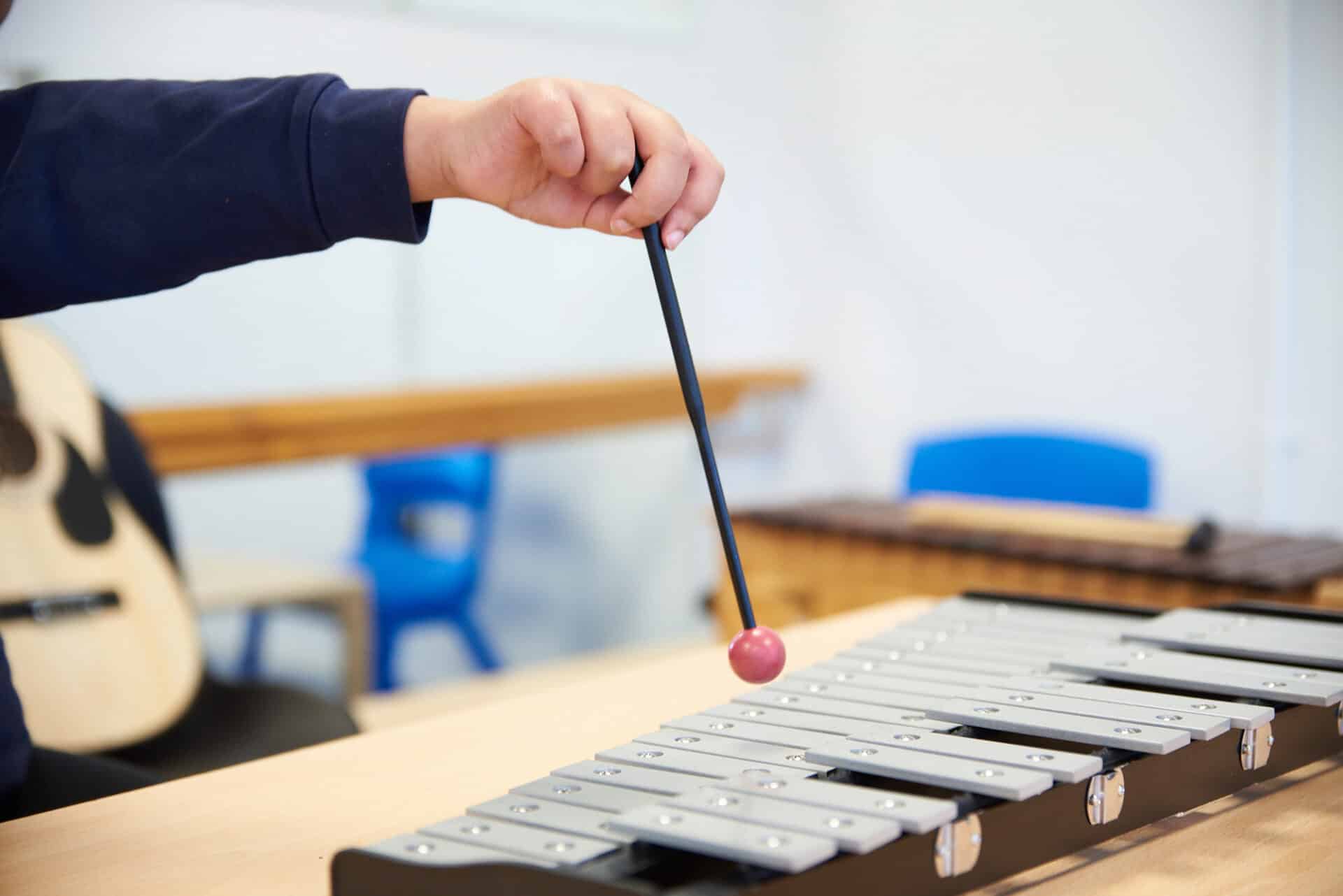 A child holds a beater above a xylophone instrument atop a table.