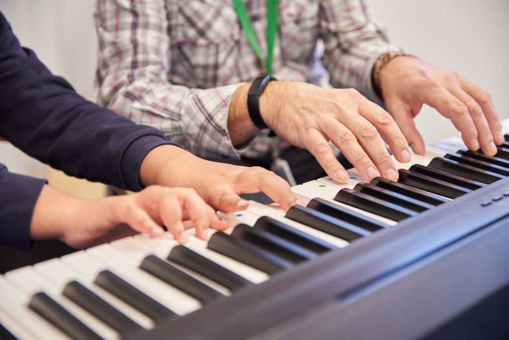 A music therapist and client put their hands on an electric keyboard during a music therapy session.
