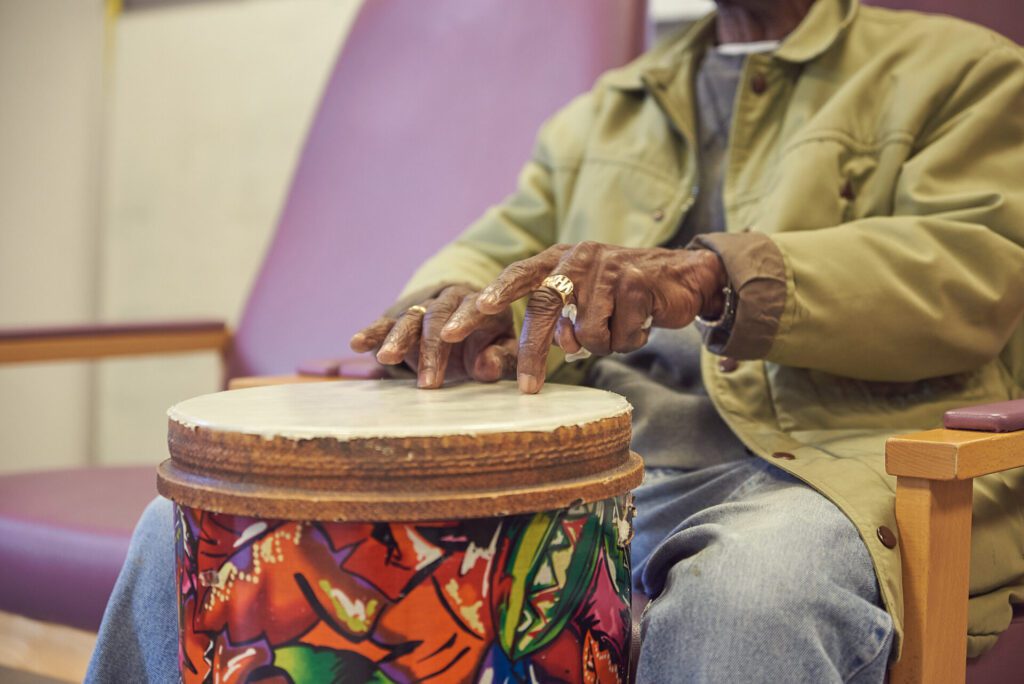 A client is seated during a music therapy session, their hands picturing playing a drum