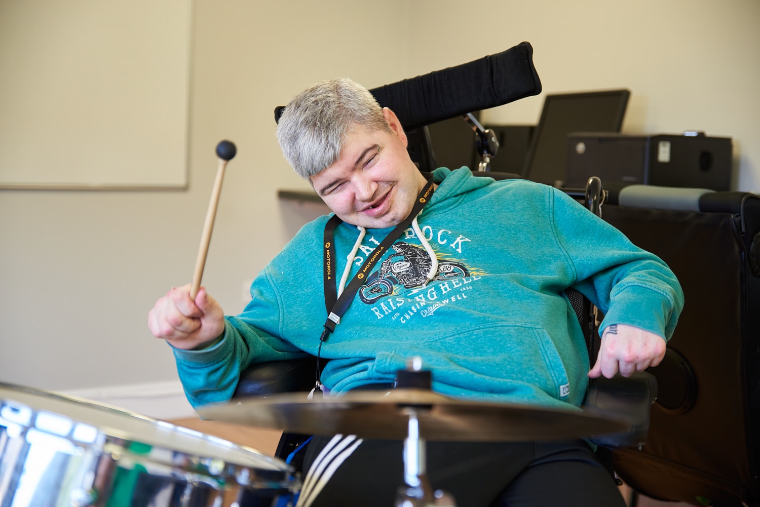 A music therapy client smiles whilst holding a drum beater