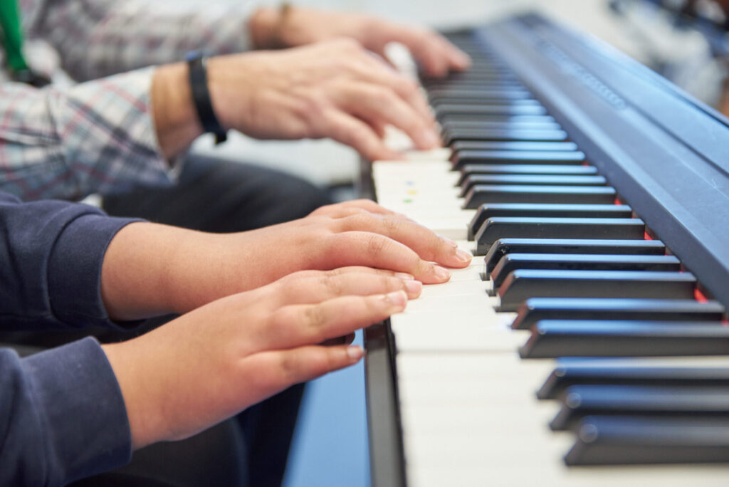 A pupil at one of our partner schools, and music therapist, play the keyboard together