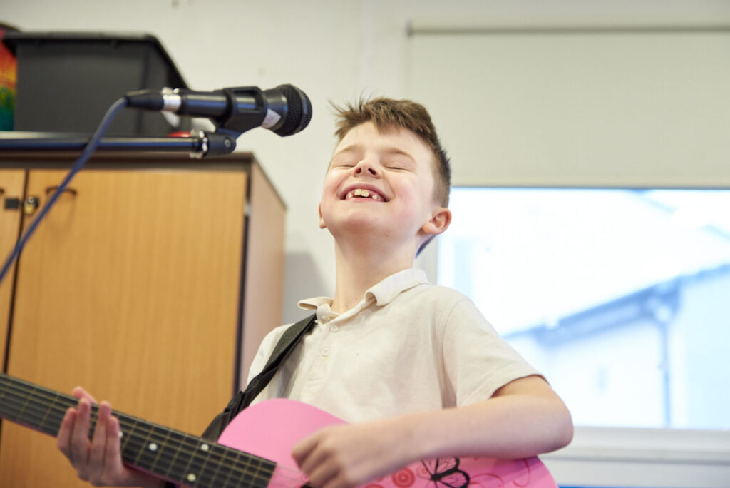 A boy playing a guitar and smiling