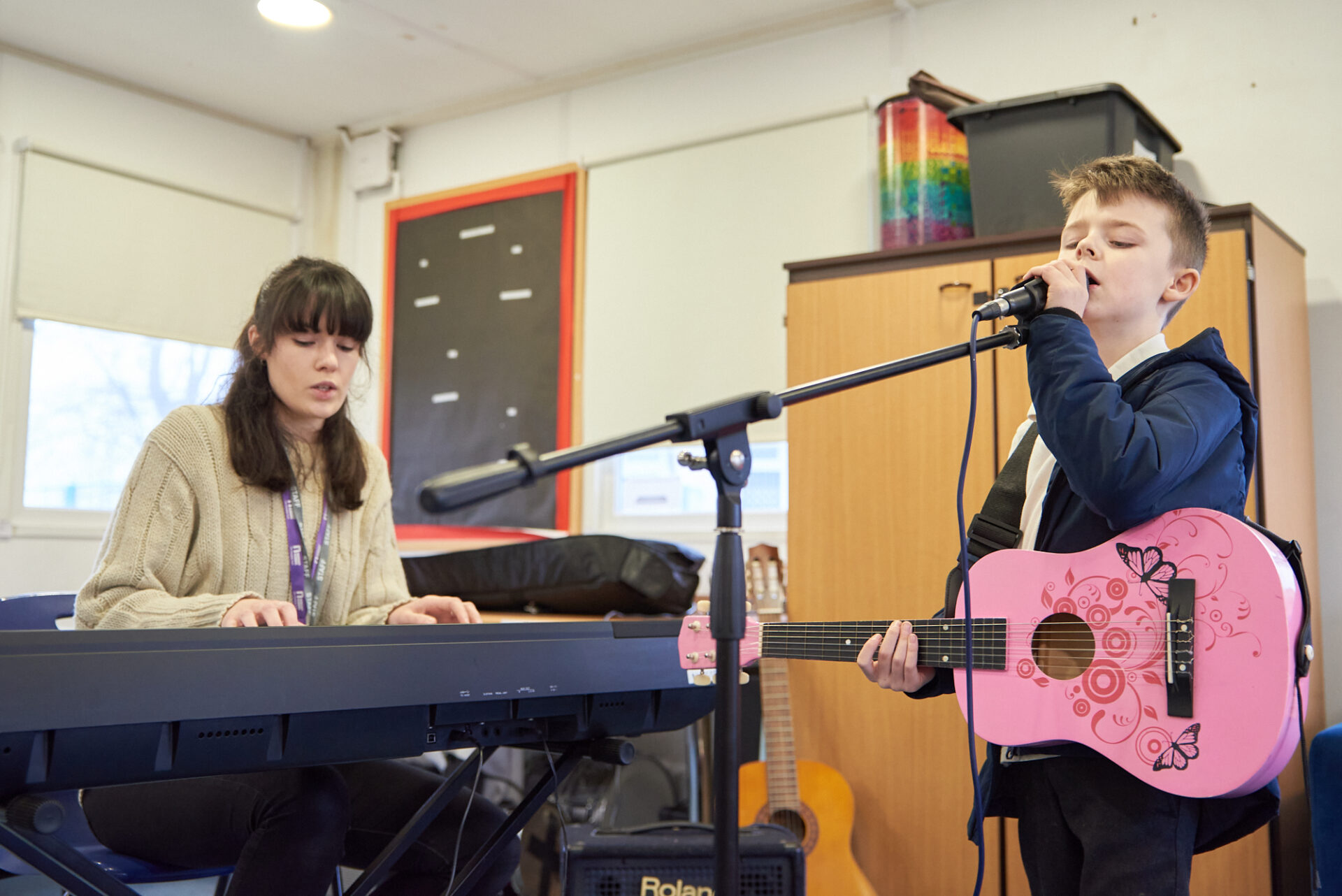 Alfie sings into a microphone during a music therapy session, whilst music therapist Charlie plays the keyboard.