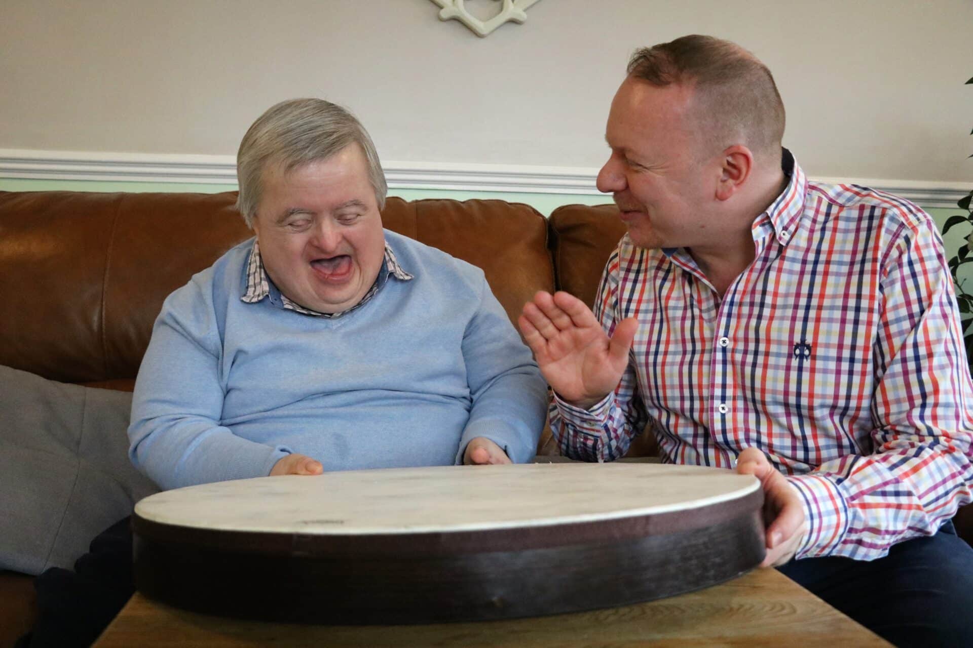Alan playing the drum with a client. They are both laughing together as Alan hits the drum.
