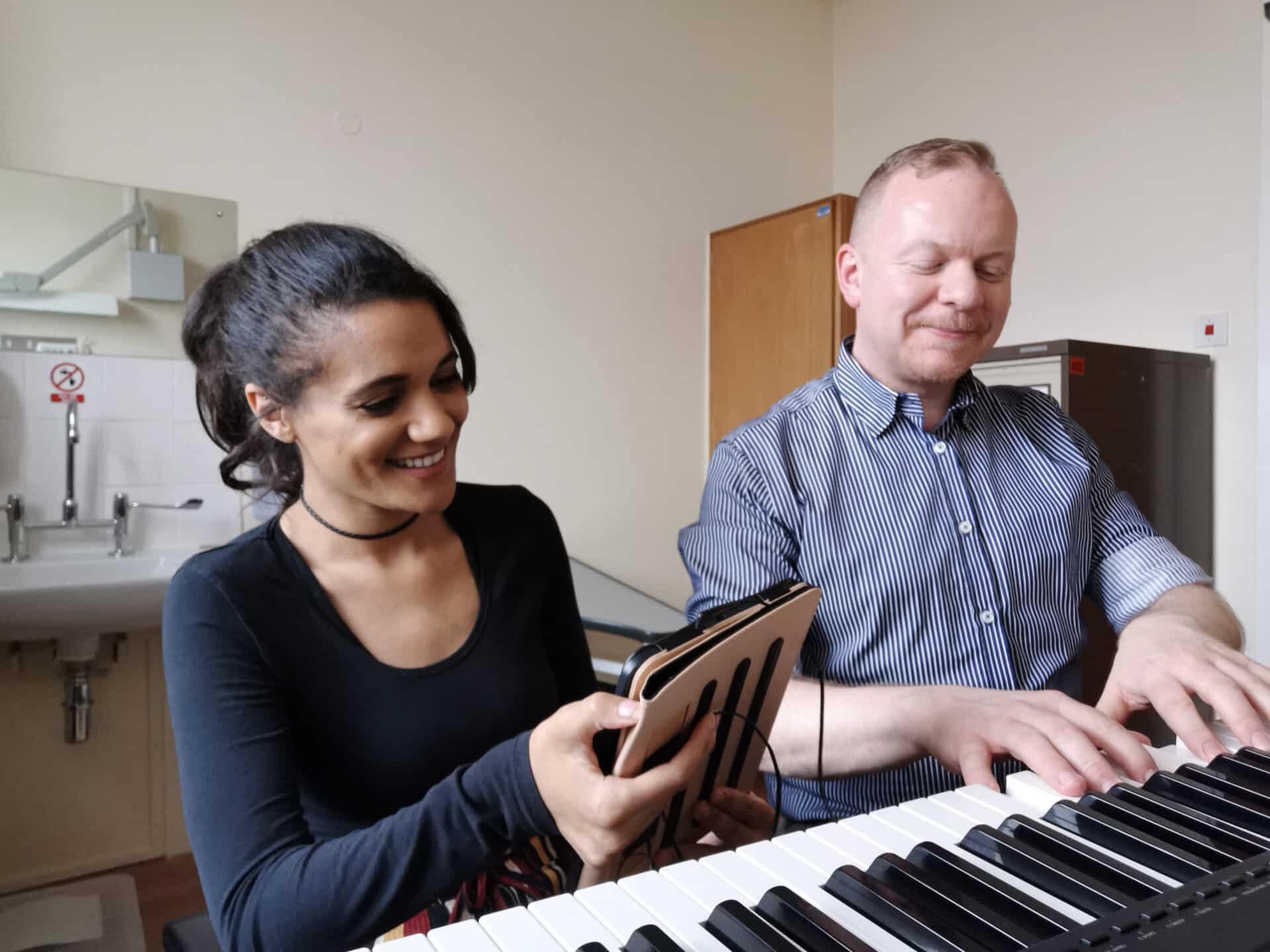 Alan playing the piano with a client who is smiling and singing along.