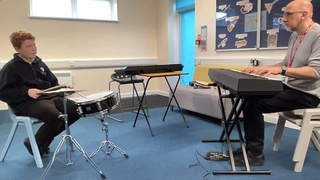 Freddie plays the drum and symbol in a music therapy session with Fraser.