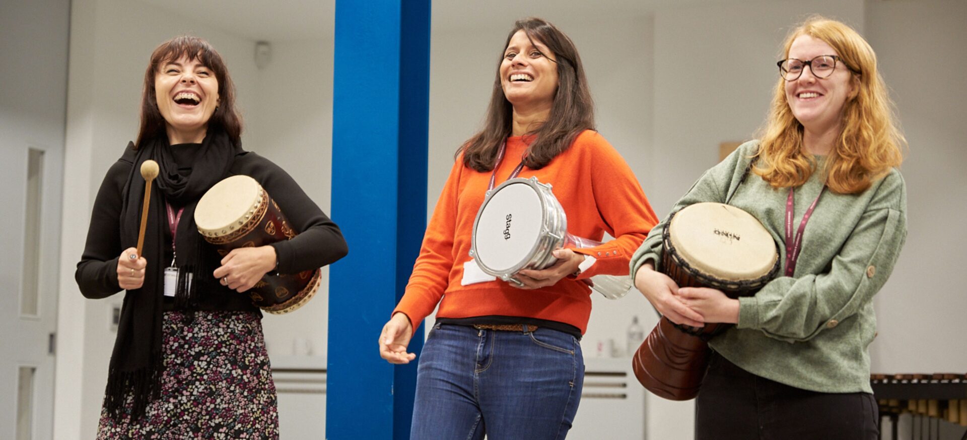 Three women stood together playing musical instruments and looking like they're having a great time