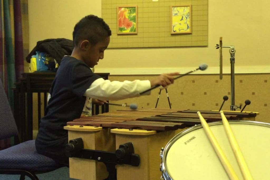 Jamal, when he was a child, is playing the xylophone in a music room